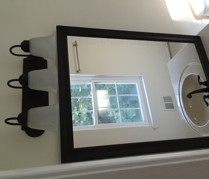 A mirror in a bathroom with a window behind it.