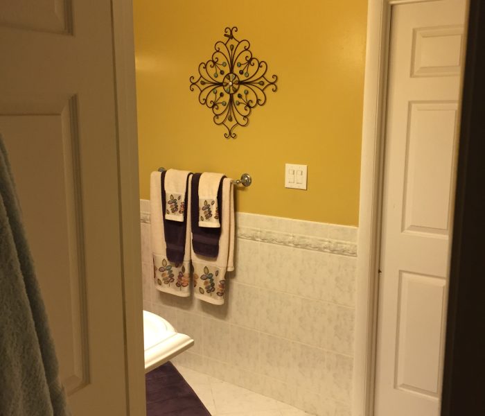 A bathroom with a yellow wall and a purple rug.