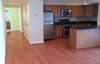 An empty kitchen with hardwood floors and stainless steel appliances.