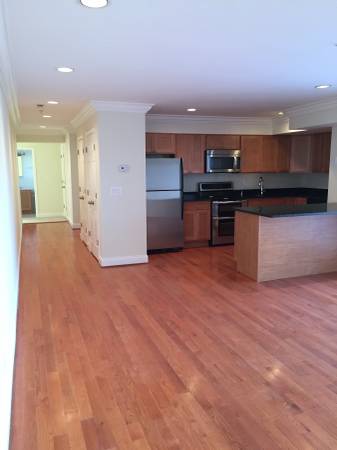 An empty kitchen with hardwood floors and stainless steel appliances.