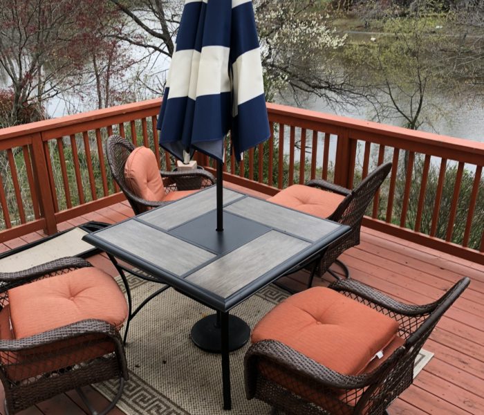 A table and chairs on a deck with an umbrella.