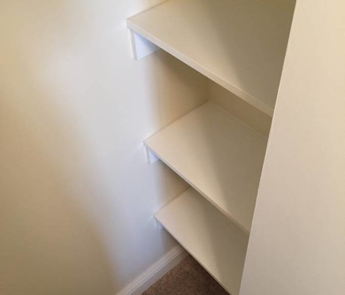 A white closet with shelves in the corner.