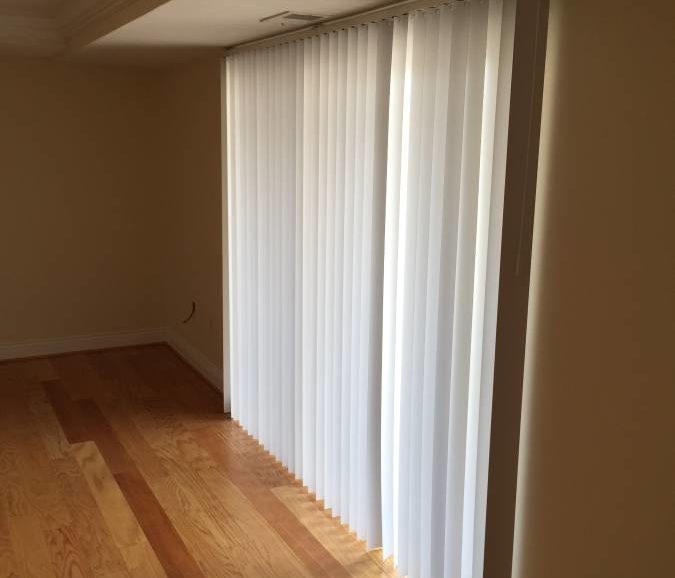An empty room with white blinds and hardwood floors.