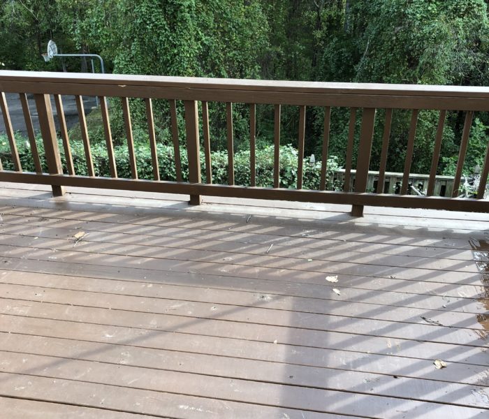 A wooden deck with a railing and a tree in the background.
