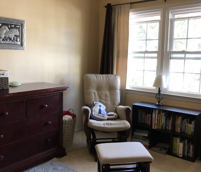 A baby's room with a rocking chair, a dresser, and a window.